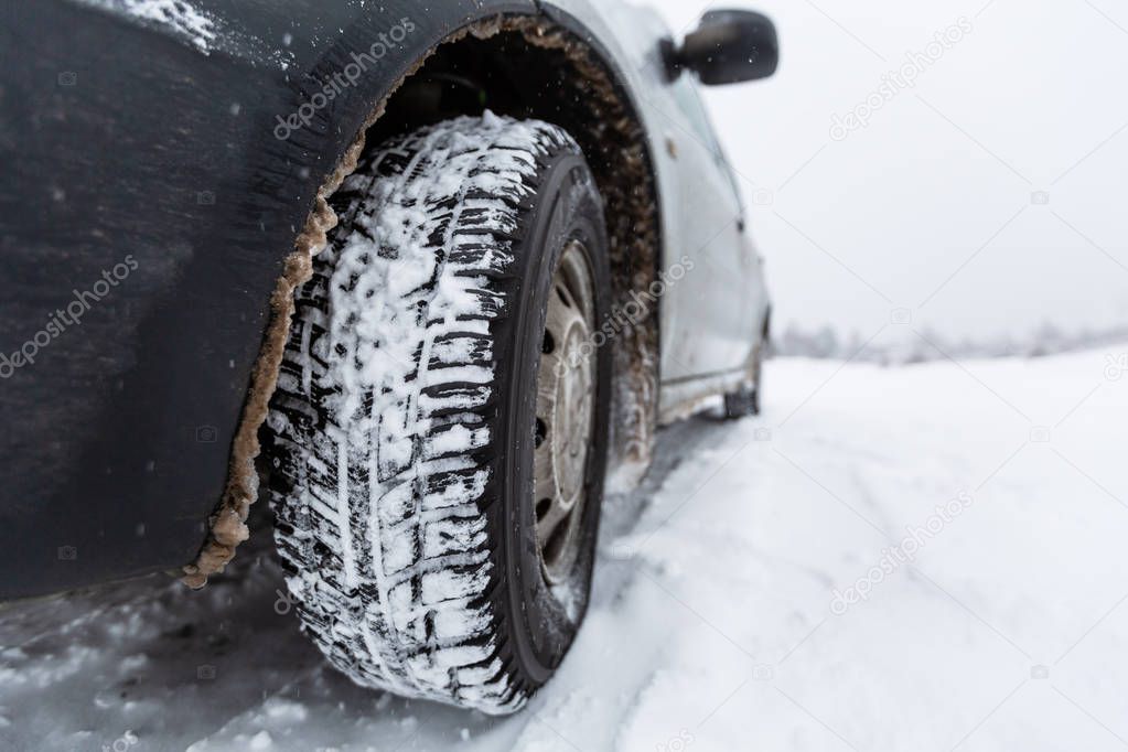 View focused on the car tire and  bumper  on winter road covered with snow. Vehicle on snowy road after snowfall.
