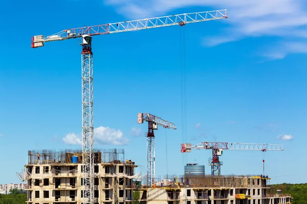 Large construction site including several cranes working on a building complex, workers, construction gear, tools and equipment, and    sky as background.