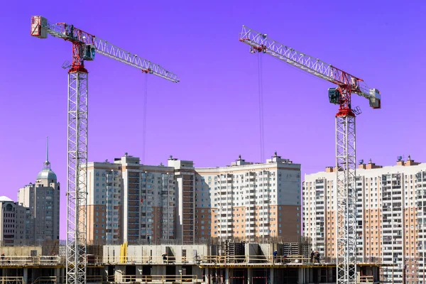 Large construction site including several cranes working on a building complex, workers, construction gear, tools and equipment, and    sky as background.