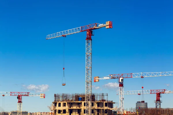 Large construction site including several cranes working on a building complex, workers, construction gear, tools and equipment, and    sky as background.