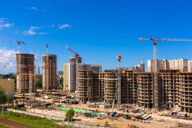 Bir bina kompleksi, işçi, inşaat dişli, araç ve ekipman, kamyon ve arka plan olarak berrak mavi gökyüzü üzerinde çalışan birkaç vinçler de dahil olmak üzere büyük şantiye.