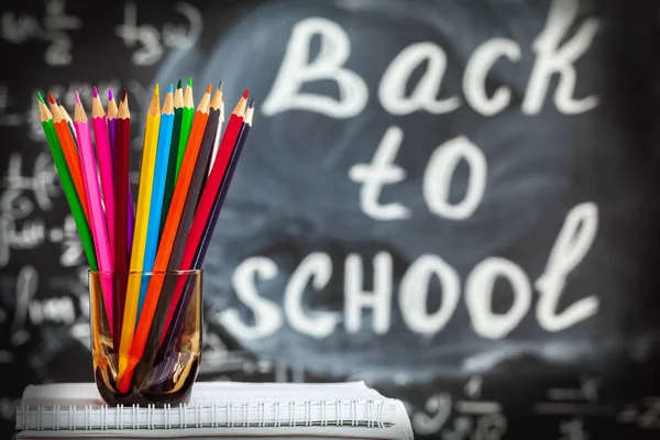 Назад в школу на фоне цветного карандаша и названия, написанного белым шальком на черной школьной доске — стоковое фото