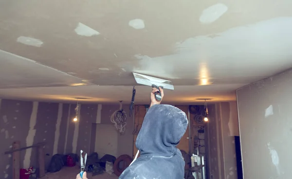 工人正在用调色板刀从公寓房间的木平台上压平天花板, 是电脑施工、改造、翻新、大修、扩建、修复和 — 图库照片