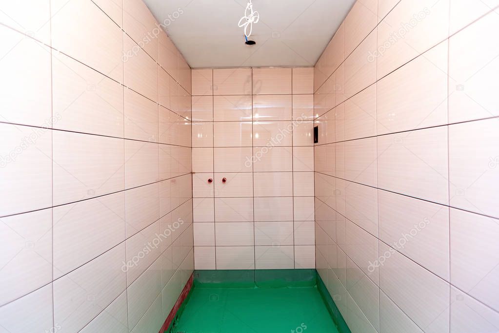 Bathroom with tiled walls and floor painted by green colored waterproof finish material in apartment is inder construction, remodeling, renovation, overhaul, extension, restoration and reconstruction