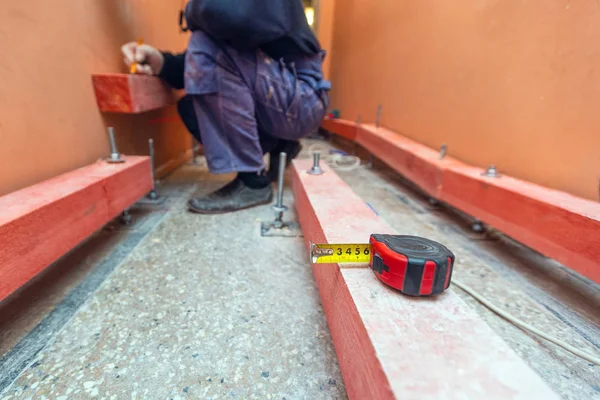 Tape-measure on the wooden block and worker in apartment that is under construction, remodeling, renovation, extension, restoration and reconstruction. Concept of total home improvement.