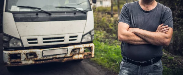 Mężczyzna kierowca w staromodny t-shirt skrzyżował ręce i pozostaje w pobliżu jego stary zardzewiały samochód na parkingu. — Zdjęcie stockowe