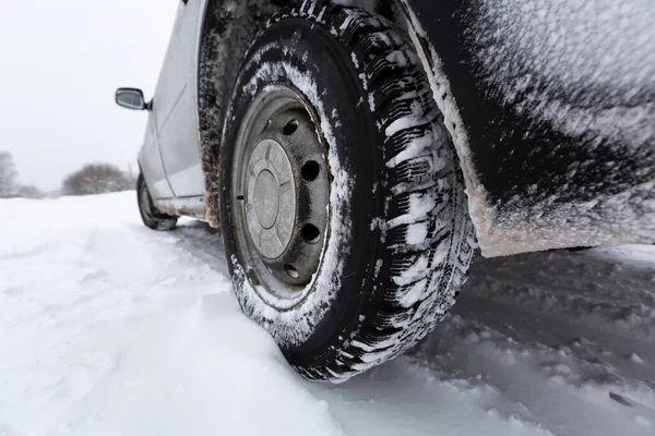Вид сфокусирован на автомобильных шинах и заднем бампере на покрытой снегом зимней дороге. Автомобиль на снежной дороге после снегопада . — стоковое фото