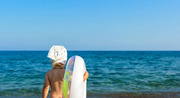 Petite fille restant avec anneau flottant ou anneau gonflable sur la plage sur la côte bleue de la mer, regardant vers le ciel et prêt à nager. Concept de vacances d'été ou de vacances . — Photo