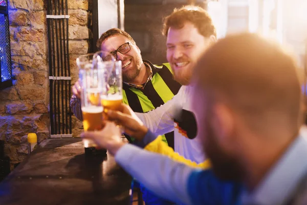 happy soccer fans drinking beer in pub and clinking glasses