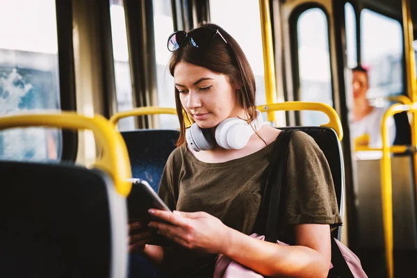 young adorable woman sitting on bus seat listening to music and drinking coffee