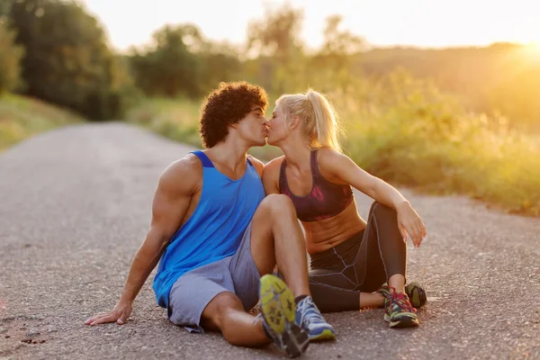 Sporty handsome fit couple sitting in a park after training and kissing.