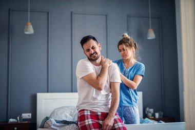 worried man holding his neck after sleep while his wife helping with massage clipart