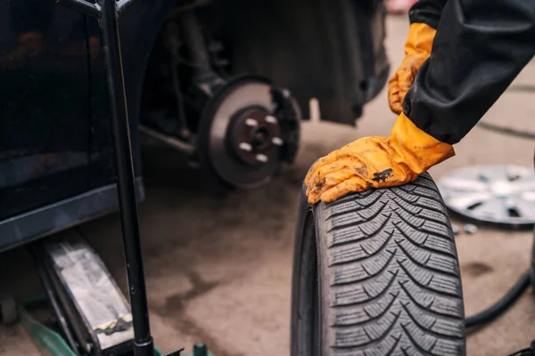 Picture of auto mechanics hands putting car tire on cr in workshop.