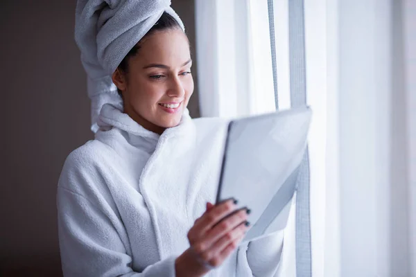 beautiful woman in robe smiling after shower and using tablet pc