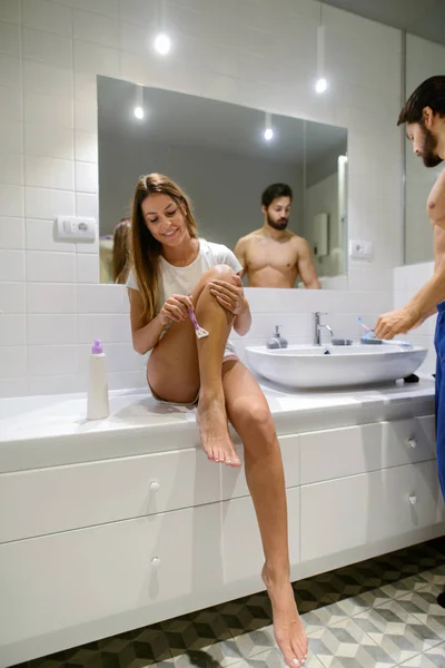 美しい少女は 彼女の夫は彼を準備する自己作業しながら彼女の足をシェービングです 浴室で一緒に立っています — ストック写真