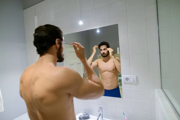 浴室の鏡の前で髪型を作る筋肉のひげを生やした上半身裸の男 — ストック写真
