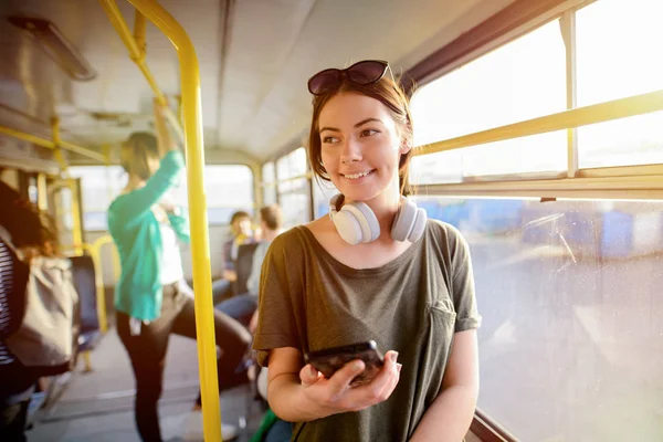现代微笑可爱的女孩站在公共汽车上 脖子上挂着耳机 微笑和望向远方 — 图库照片