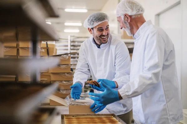新鮮な手作りのクッキーを梱包し 楽しい時を過して無菌服で つ男性食品工場の従業員の写真 — ストック写真