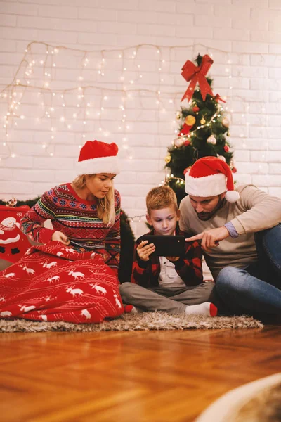 幸福的家庭庆祝圣诞节在家坐在地板附近的圣诞树和赠送礼物给对方 小儿子玩平板电脑 — 图库照片