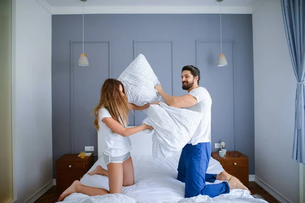 Beautiful young woman and man pajamas having fun in bedroom and fighting with pillows