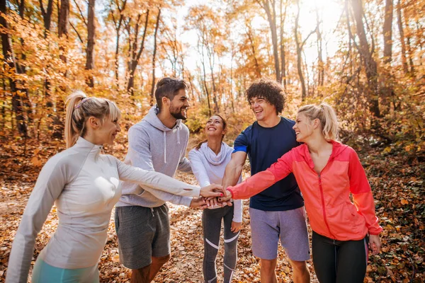 Small group of runners putting hands on hands and smiling. Woods in autumn exterior. Teamwork concept.