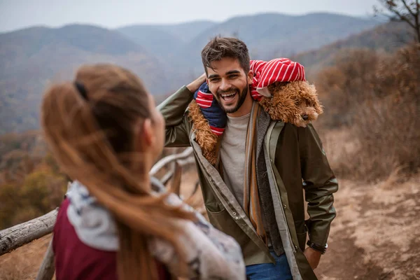 男子站在那里 肩膀上挂着狗 和女友说话 有选择地关注人 在背景山和森林 秋天时间 — 图库照片