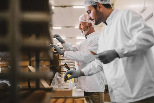 Imagem Dois Funcionários Fábrica Alimentos Masculinos Roupas Estéreis Embalando Biscoitos — Fotografia de Stock
