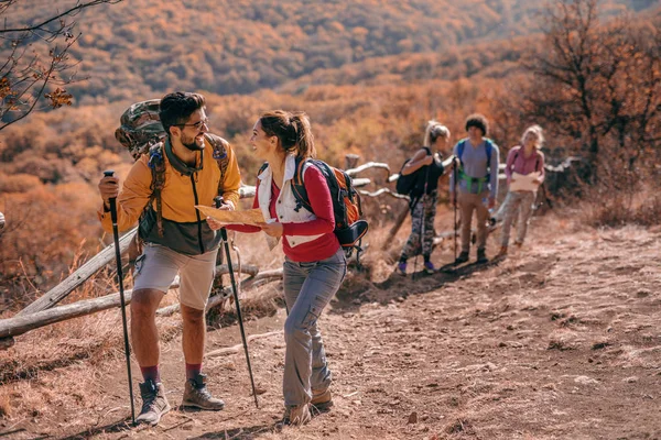 Couple climbing the hill and talking. Woman holding map. In background their friends. Autumn season, adventure concept.