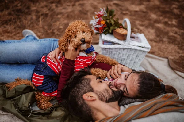 一对夫妇在野餐躺在毯子上与他们的狗和拥抱 在他们旁边野餐篮秋季时间 — 图库照片