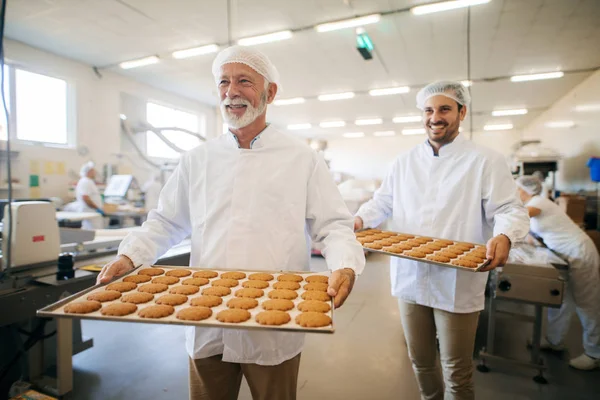 食品工場のプレートでクッキーを運ぶ二人の男 — ストック写真