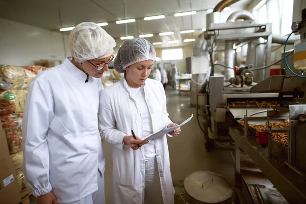 Две Работницы Контролируют Качество Продуктов Питания Пищевой Фабрике Один Держит — стоковое фото