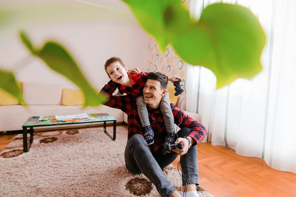 欢快兴奋的父亲和小儿子在红衬衫玩游戏机与游戏板 — 图库照片