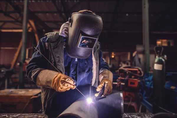 Worker welding iron. Protective suit and mask on. Workshop interior.