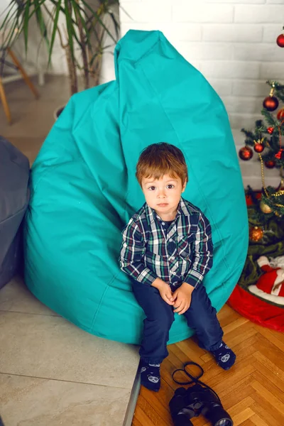 かわいい白人少年ベンの袋に座っている カメラ目線します 彼のクリスマス ツリーの横にあります — ストック写真