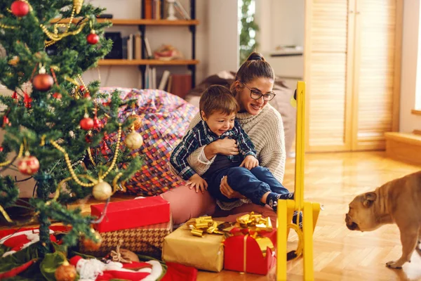 母亲和儿子坐在地板上和狗玩 旁边是圣诞树和礼物 家居内饰 圣诞节假期概念 — 图库照片