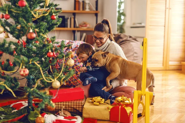엄마와 아들이 바닥에 앉아있는 강아지와 그들에 크리스마스 트리와 인테리어 크리스마스 — 스톡 사진