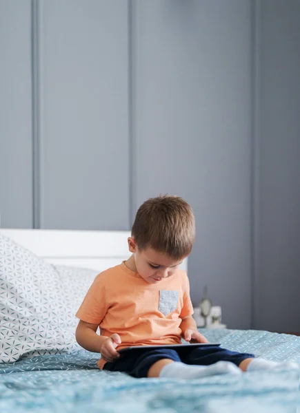かわいい好奇心幼児少年タブレット をベッドの上に座って ビデオ ゲームをプレイ — ストック写真