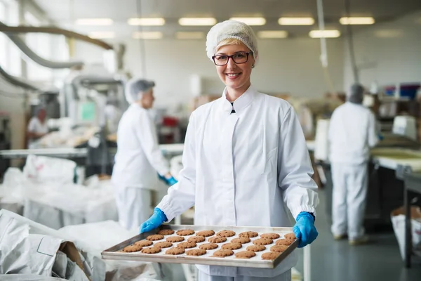 立っていると クッキーのプレートを保持している女性労働者 食品工場の内部 — ストック写真