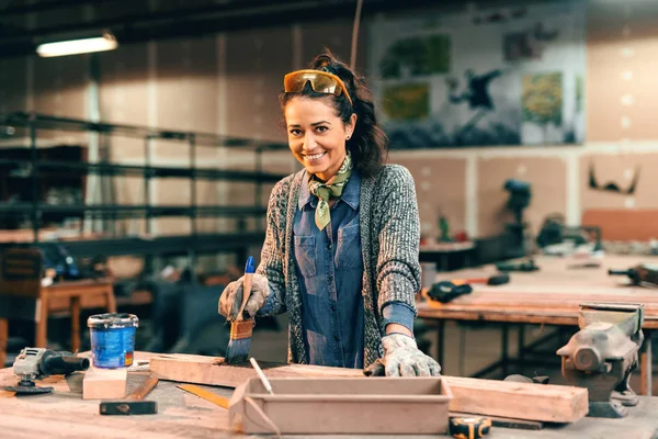 Woman painting board with black wood paint, smiling.