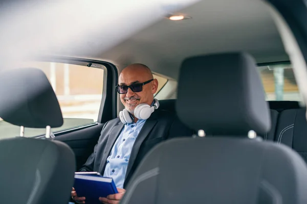 首と手の議題の周りのイヤホンで車の後部座席に座って幸せなひげを生やしたシニア大人ビジネスマン — ストック写真