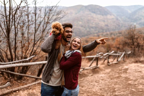 自然にハグのカップル 男は何かを指していると犬を彼の肩につかまって 秋の時間 — ストック写真