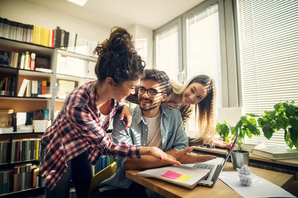 Two cheerful student girls helping their friend to pass the exam.Sitting in a bright library.