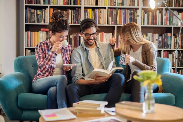 Tres Estudiantes Sonrientes Sentados Sofá Biblioteca Mirando Libro —  Fotos de Stock