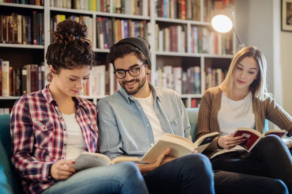 Три Студенти Читають Книги Сидячи Дивані Бібліотеці Фоновій Книжковій Полиці — стокове фото