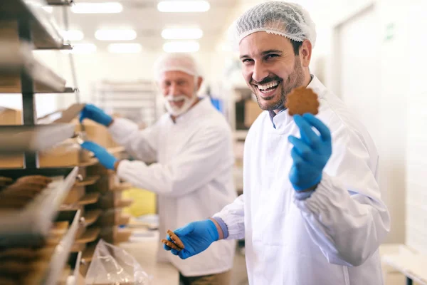 Junge Lächelnde Kaukasische Arbeiterin Zeigt Kekse Während Sie Der Lebensmittelfabrik — Stockfoto