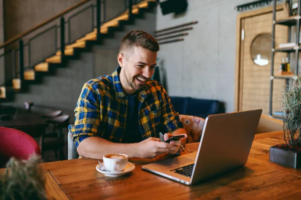 Uśmiechający Się Brodaty Kaukaska Freelancer Trzymając Smartfon Patrząc Laptopa Kawa — Zdjęcie stockowe