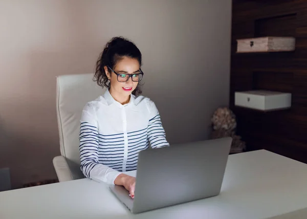 Hard working Caucasian female employee with eyeglasses working on laptop while sitting in office. White color dominating.