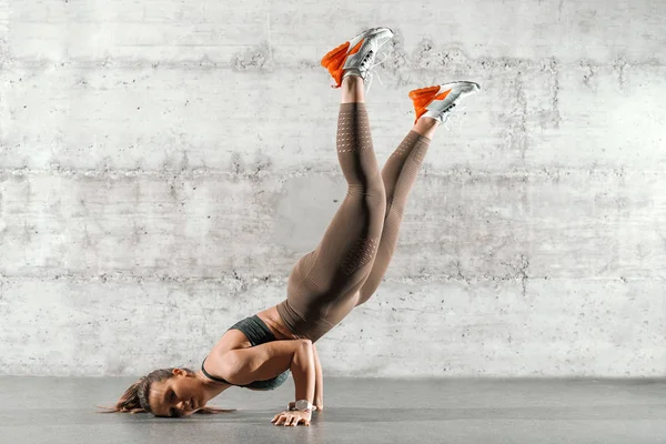 筋肉の側面図に合わせてブルネット ポニーテールと灰色の壁の前で倒立をやってスポーツウェア — ストック写真