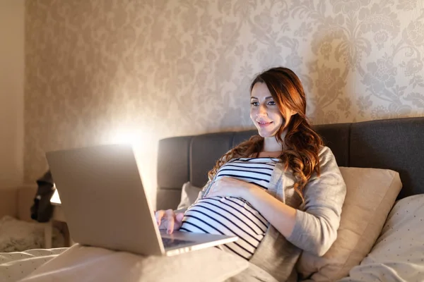 Sonriendo Hermosa Mujer Embarazada Acostada Cama Sosteniendo Vientre Mientras Usa —  Fotos de Stock