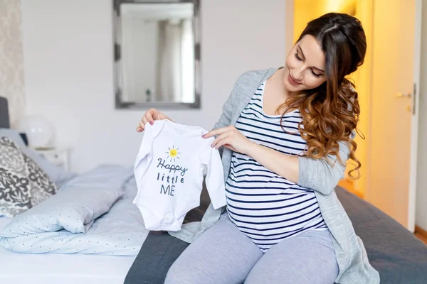 Sonriente Morena Embarazada Con Pelo Largo Blusa Rayas Sosteniendo Ropa —  Fotos de Stock